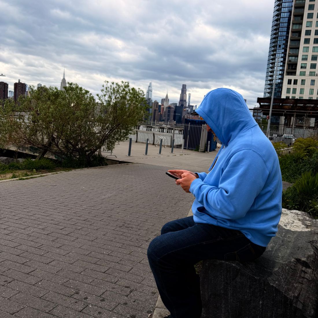 Mężczyzna w niebieskiej bluzie z telefonem, w tle Manhattan